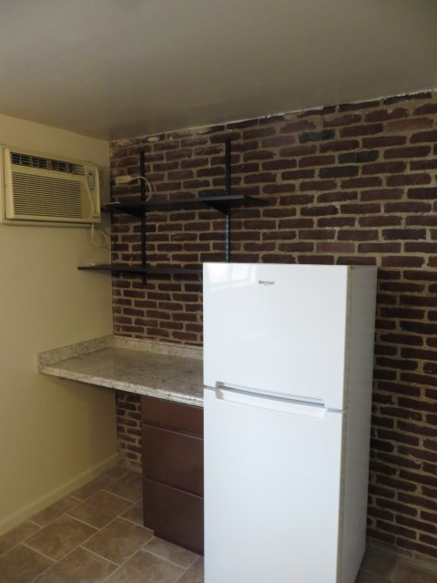 View of fridge/freezer, desk, and through wall air conditioner.